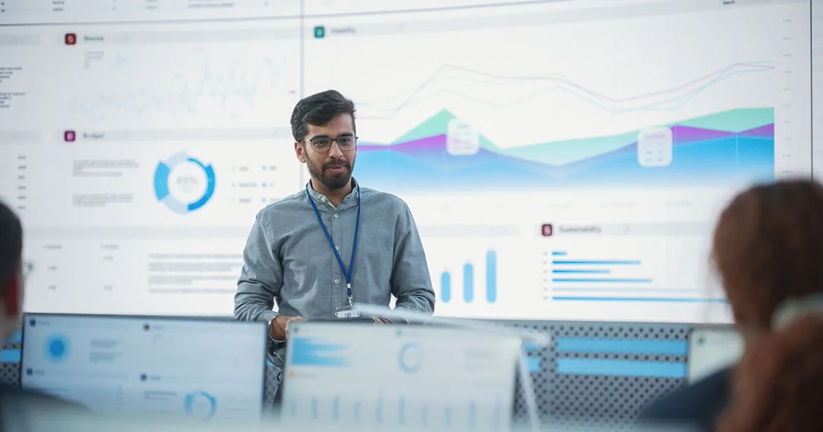 A data analyst presents insights on a large screen displaying charts and graphs, representing data-driven decision-making and analytics.
