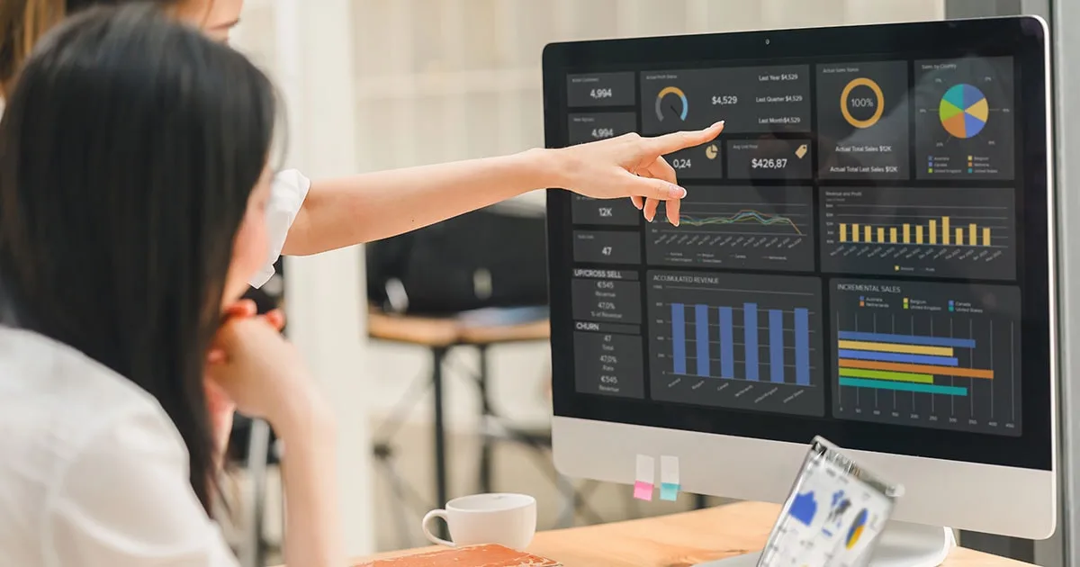 Two professionals analyse a computer screen displaying data visualisations, charts, and metrics, representing business data analytics insights.