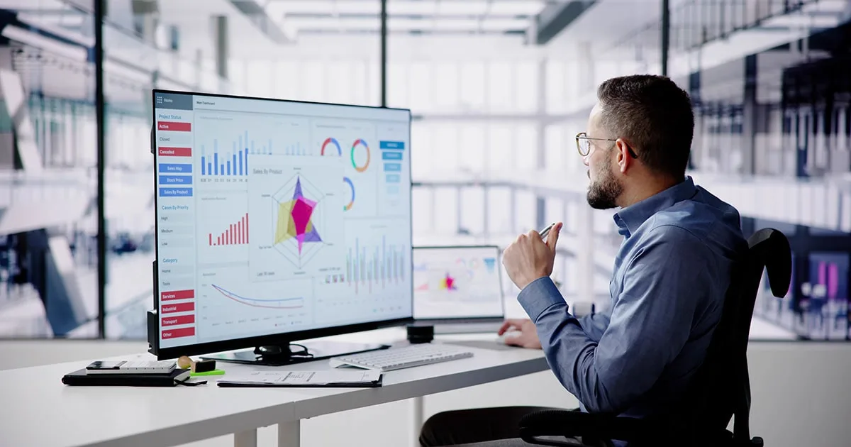 A business analyst reviews data visualisations on a large monitor, displaying charts and graphs for performance tracking and decision-making.